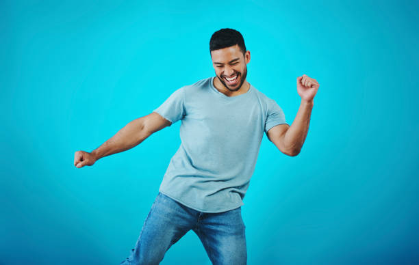 shot of a handsome young man dancing against a blue background - dancing imagens e fotografias de stock