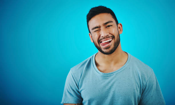 Shot of a handsome young man posing against a blue background Don't take me too seriously human tongue stock pictures, royalty-free photos & images