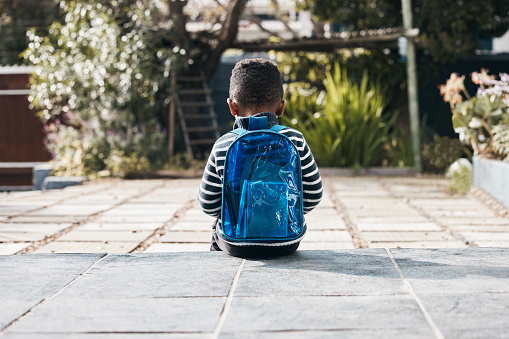 Shot of a little boy sitting outside with his backpack
