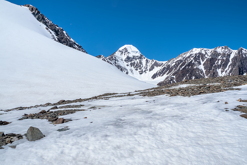 Snowfields on a mountain slope. Dangerous cliff. Atmospheric scenery on top of mountain ridge. Snowy high-altitude plateau. Scenic view from precipice edge under blue sky to snowy mountains.