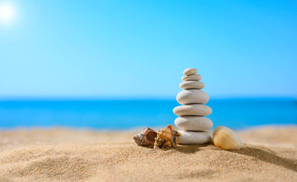 tour de galets avec de petits coquillages sur la plage ensoleillée avec en toile de fond la mer. thème de l’été. - pebble sand photos et images de collection