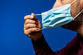 Detail of face of hispanic man taking off his surgical mask isolated on blue background, he gets rid of the mask astied from the desperate situation of the new normal caused by the coronavirus
