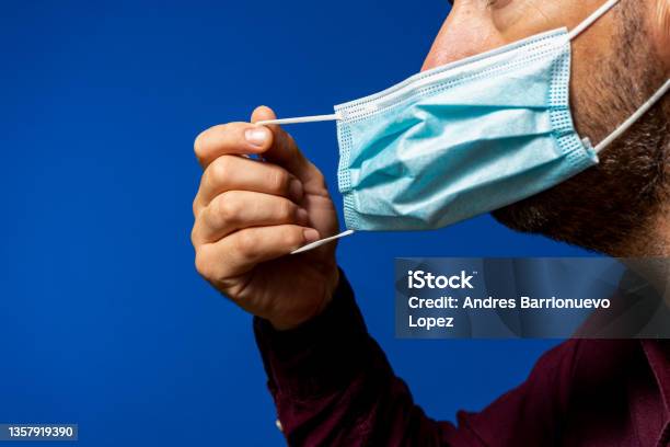 Detail Of Face Of Hispanic Man Taking Off His Surgical Mask Isolated On Blue Background He Gets Rid Of The Mask Astied From The Desperate Situation Of The New Normal Caused By The Coronavirus Stock Photo - Download Image Now