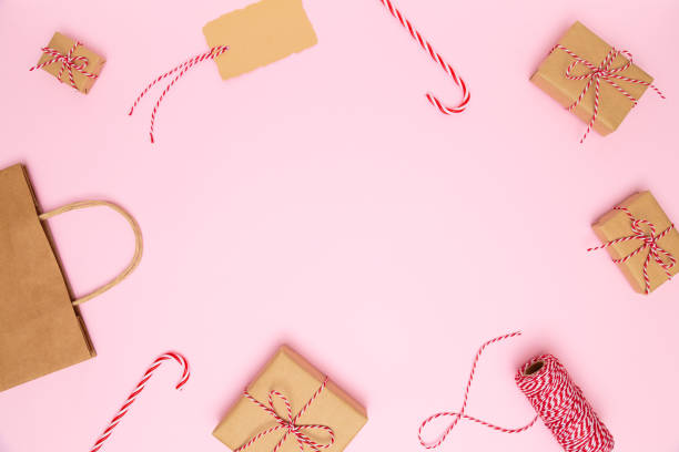 Christmas, New Year cozy background. Handmade craft gift boxes with red bows, paper bag, candy canes, red ribbon, note card on pastel pink background. Preparation for holidays. Flat lay, copy space navidad, año nuevo fondo acogedor. cajas de regalo artesanales hechas a mano con lazos rojos, bolsa de papel, bastones de caramelo, cinta roja, tarjeta de notas sobre fondo rosa pastel. preparación para vacaciones. colocación plana, espacio de copia