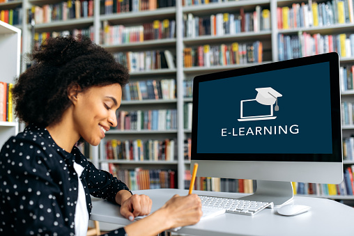 Online training, distance learning concept. African American teenage female student, sits at a desk, taking notes during online studying, smiling. Online class during quarantine