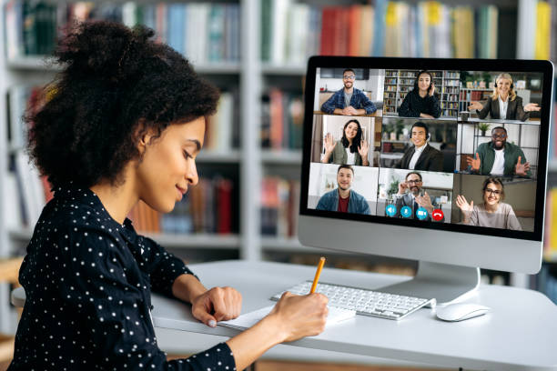 istock Video call, online conference using app and computer. African American female student, studying remotely, watches an online lecture, taking notes, multiracial smiling people on the computer screen 1357921499