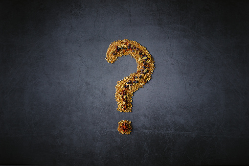 Question mark made of spices on dark grunge background. The spices are tonka bean, coriander, anise star, cardamom, and clove. Copy space. Color editing with added grain.