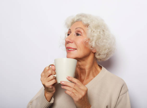 istock old excited lady smiling laughing, holding cup drinking coffee, tea, over white background 1357930320