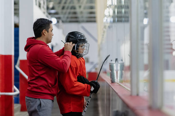 vater hilft seinem sohn, sich auf das training vorzubereiten - ice skating ice hockey child family stock-fotos und bilder