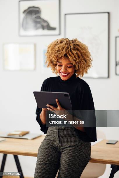 Happy Businesswoman Sitting On Her Desk Using Her Tablet Stock Photo - Download Image Now