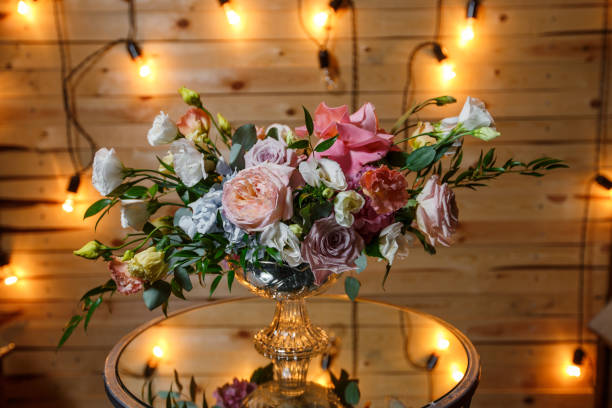 istock Delicate and very beautiful wedding bouquet of roses, greenery, eustoma standing on mirror table. Bridal trendy flowers in pastel colors on the background of the evening lighting bulbs. 1357940643