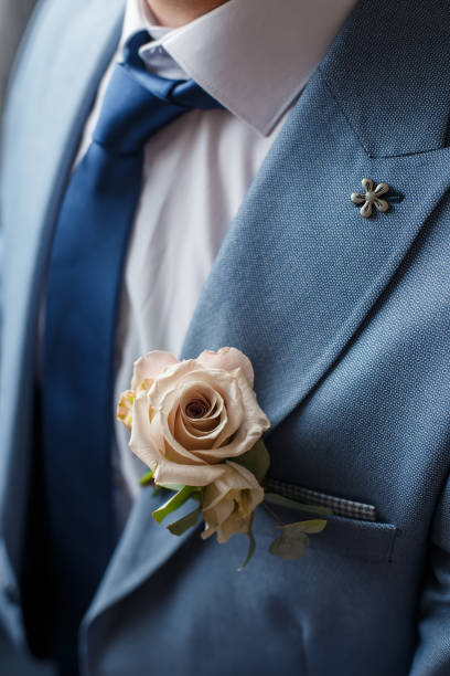 Boutonniere of beige rose flower and greenery attached to the blue suit of groom. Wedding details and floristics. Boutonniere of beige rose flower and greenery attached to the blue suit of groom. Wedding details and floristics dinner jacket stock pictures, royalty-free photos & images