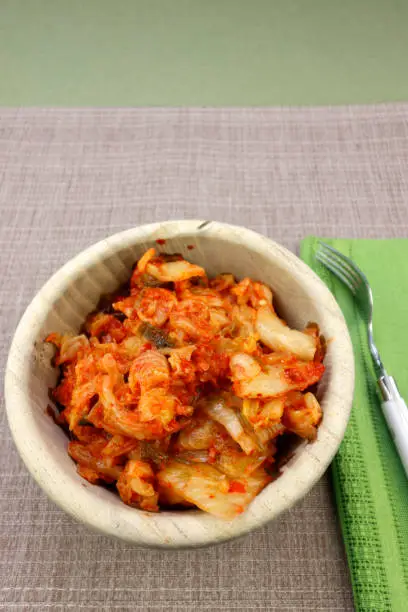 In a wooden bowl ready to eat with a fork is fermented kimchi made with napa cabbage and radish. Flavorful fermented napa cabbage with radish and aromatic seasonings kimchi recipe in a wooden bowl.