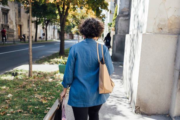 a back view of an anonymous female going home after work with lots of paper bags - green friday stockfoto's en -beelden