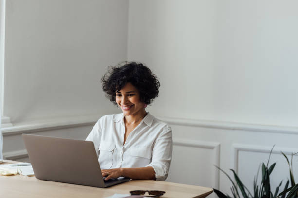 une belle femme métaite travaillant en ligne à domicile sur son ordinateur portable - simplicity using computer women computer equipment photos et images de collection