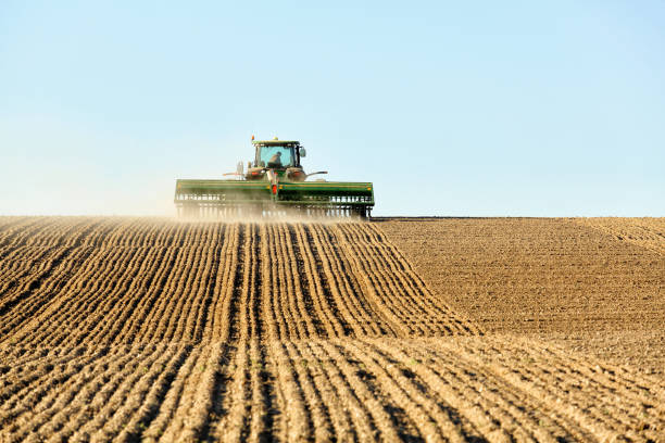 A tractor and planting implement creates a dust cloud while planting a wheat field in the fertile farm fields of Idaho.