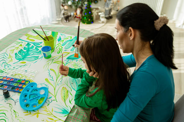 istock While paint with watercolors, creative girl sitting in mother lap 1357954279