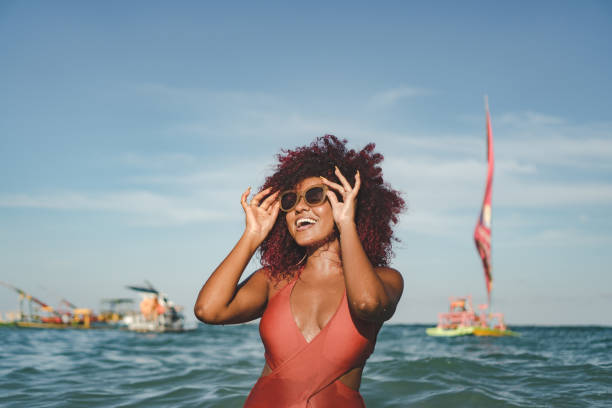 istock Afro woman using sunglasses on the beach 1357954363