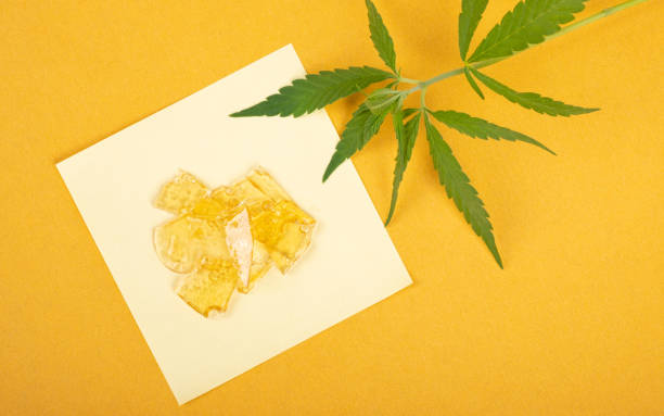 amber drops of cannabis wax with green marijuana leaf close-up, resin high in thc on a yellow background stock photo