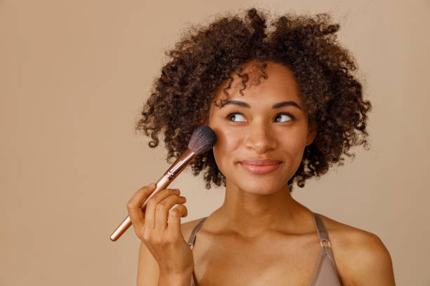 istock Cute lady using cosmetic brush over beige background 1357956354