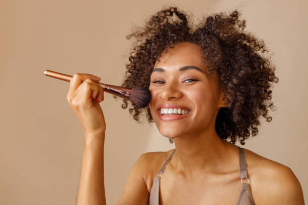 Charming woman demonstrating makeup tool against beige wall stock photo