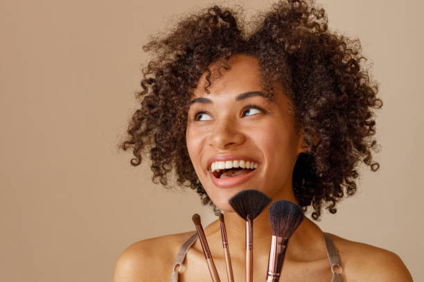 istock Cheerful woman demonstrating makeup tools against beige wall 1357956365