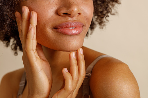 Cropped shot of multiracial young woman, touching face and enjoying beauty when posing against beige background