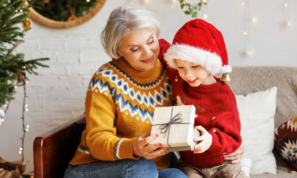 冬休み中に笑顔の祖母にクリスマスギフトボックスを与える小さな男の子の孫 - grandmother child senior adult multi generation family ストックフォトと画像