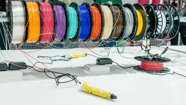 istock Blurred yellow 3D pen lying on white table, with skeins of colored plastic behind it 1357958211