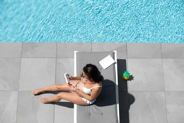 Pregnant woman at the poolside applying sun-protection cream