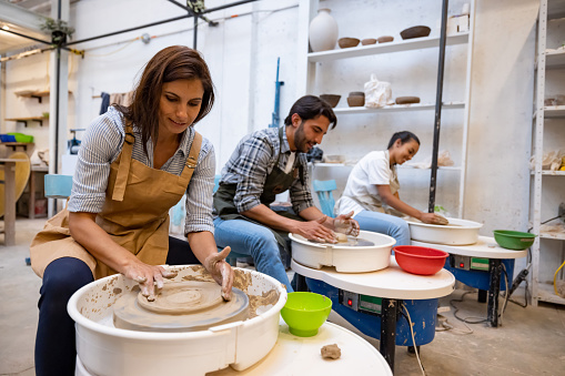 Happy group of Latin American people in a pottery class learning how to use the wheel