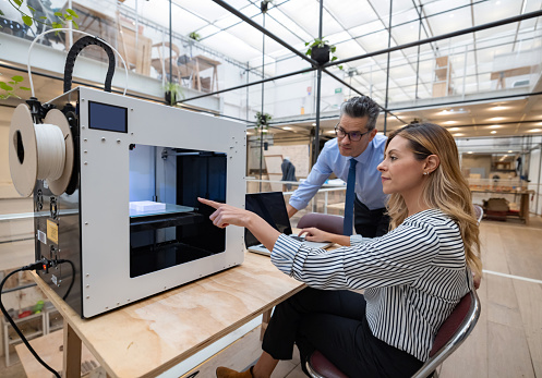 Designers printing a design on a 3D printer at the office and pointing at the machine.