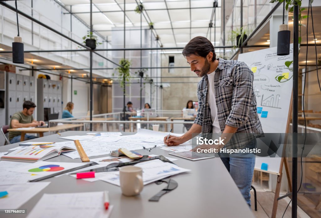 Creative business man working at a coworking space Creative Latin American business man working at a coworking space and sketching some designs. **DOCUMENTS DESIGNS ALL BELONG TO US** Fashion Stock Photo