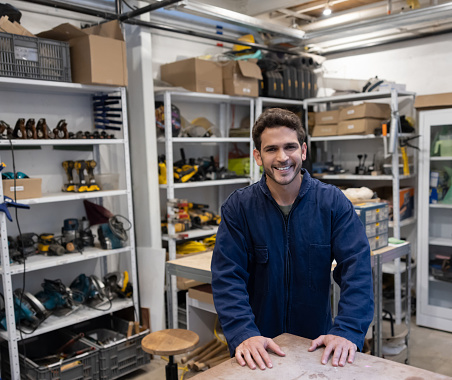 Happy Latin American carpenter smiling in the tool storage room of his workshop and looking at the camera