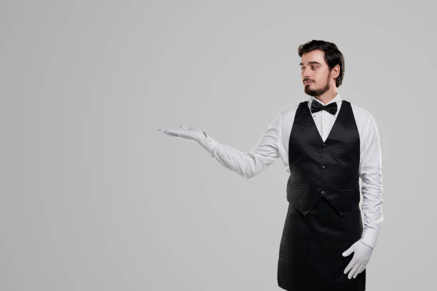 istock Elegant waiter pointing aside on blank space 1357969407
