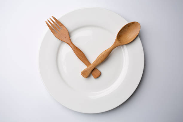 istock clock white plate with wooden spoon and fork eating time meal concept 1357970024