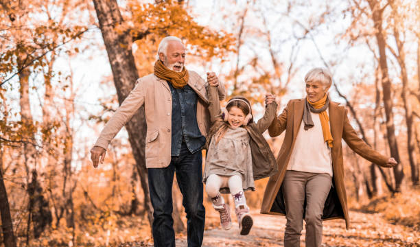 anziani felici che corrono con la loro nipotina nel parco. - family happiness outdoors autumn foto e immagini stock