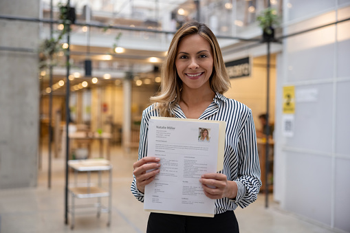 Portrait of a happy business woman holding her CV for a job interview at an office and looking at the camera smiling - recruitment concepts. **DESIGN ON ALL DOCUMENTS BELONG TO US**