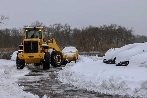 Road maintenance of snow plow tractor removing snow on parking lot for car after snowfall