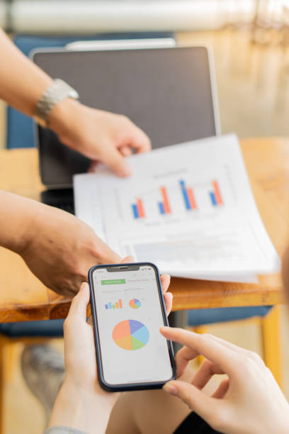 istock hand holding the phone and pointing at graph mobile screen background with a man holding a financial concept graph document 1357979947
