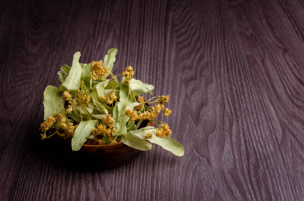 Dried linden leaves and flowers in a bowl. Wooden background. Design concept. Selective focus.