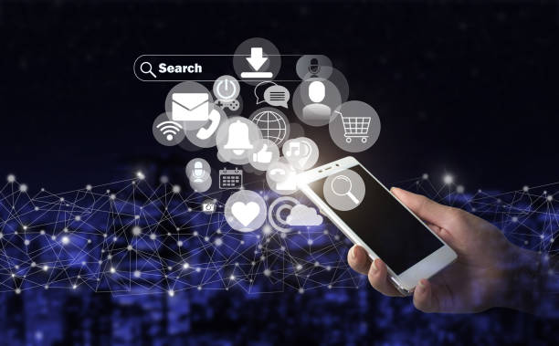 istock Social media concept. Communication network. Hand hold white smartphone with digital hologram social media icons sign on city dark blurred background. 1357997102