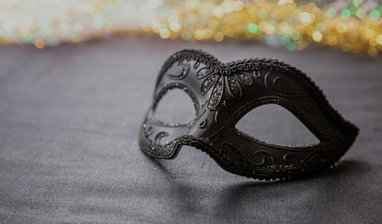 Carnival party. Venetian mask black with glitter on grey textile, shiny sparkling background. Traditional festival female disguise, masquerade