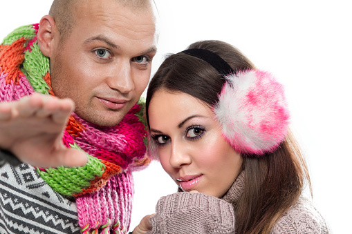 Photo of young happy attractive couple in winter clothing. Man shows something, isolated on white