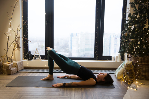 young woman meditation
and doing yoga fitness exercise  in the Christmas interior  at home. home fitness, activewear. Healthy and sport lifestyle. Christmas holidays