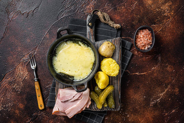 швейцарский раклет плавлен�ый сыр с отварным картофелем и ветчиной на деревянной доске. темный фон. вид сверху - raclette cheese стоковые фото и изображения