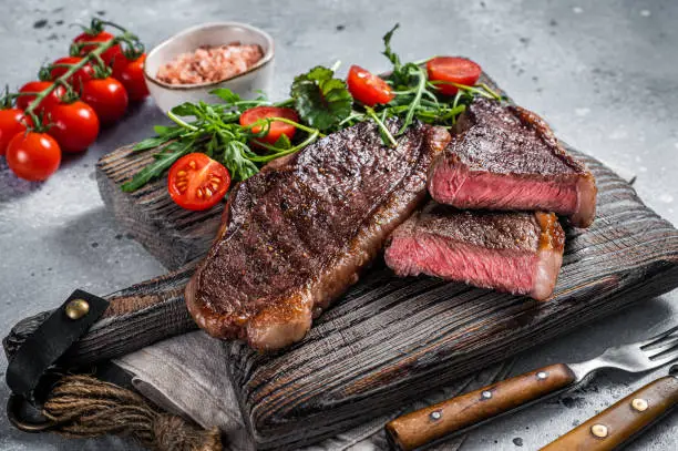 Roasted cap rump or Top sirloin beef meat steak on wooden board with salad. Gray background. Top view.