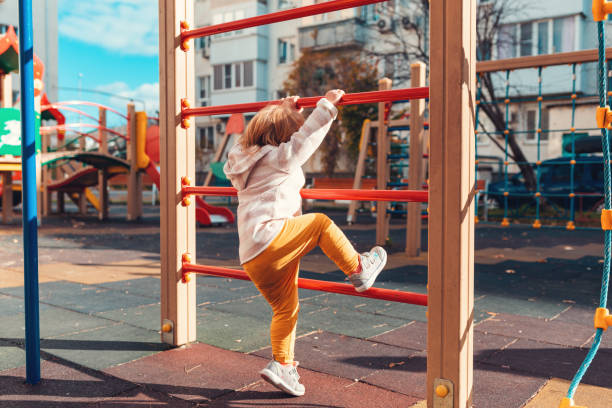un niño pequeño está escalando una pared deportiva para niños. vista desde la parte posterior. el concepto de juegos infantiles y desarrollo - parque infantil fotografías e imágenes de stock
