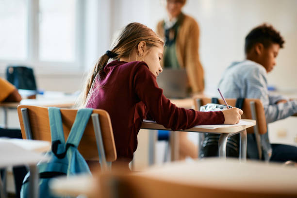 Rear view of schoolgirl writing during lecture in the classroom. Back view of student writing exam during a class at elementary school. primary school exams stock pictures, royalty-free photos & images