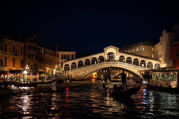Venice, Italy - October 29, 2021: Ponte di Rialto bridge in Venice by night in winter, gondola, reflections on the water